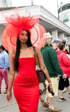 a woman in a red dress and large hat walks down the street with other people