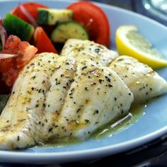 a white plate topped with fish and veggies next to a lemon wedge on top of a table