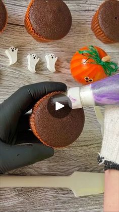 a person holding a cupcake in their hand with halloween decorations on the table behind it