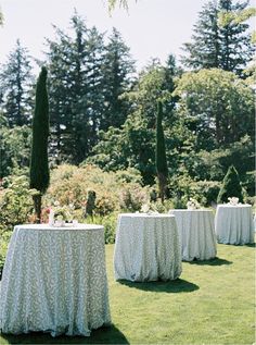 the table is covered with white cloths for an outdoor wedding reception in front of some tall trees