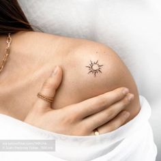 a woman's shoulder with a small tattoo on her left arm and the sun in the middle