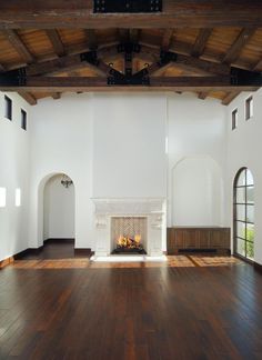 an empty living room with wood floors and fireplace in the center, surrounded by arched windows