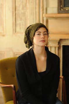 a woman sitting in a chair with her eyes closed and wearing a green head scarf