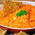 a bowl full of carrot dip with crackers on the side, and some parsley