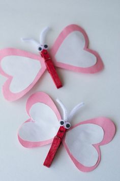 two pink and white paper butterflies with red ribbon on them, one is shaped like a heart