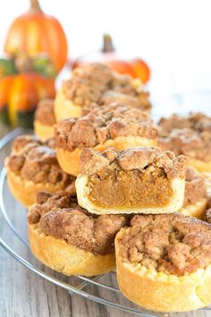 several small muffins on a wire rack with pumpkins in the back ground