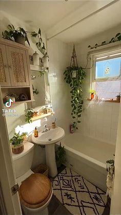 a bathroom with a toilet, sink and bathtub filled with plants on the wall