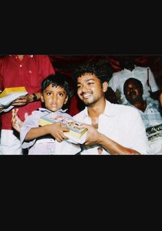 a man holding a small child in his arms while sitting down with other people behind him