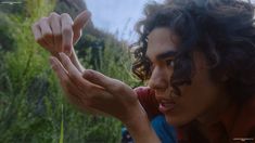 a man with curly hair holding out his hand to touch the grass in front of him