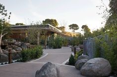 an outdoor area with large rocks, trees and a building in the background at sunset