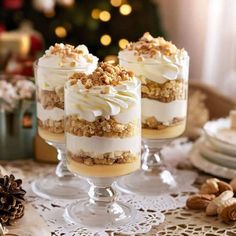 three desserts with white frosting and nuts on a table next to a christmas tree