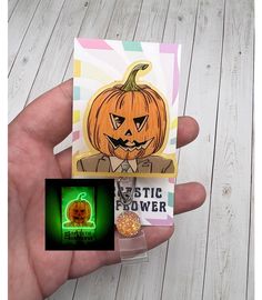 a hand holding a card with a pumpkin on it and a glow in the dark sticker next to it