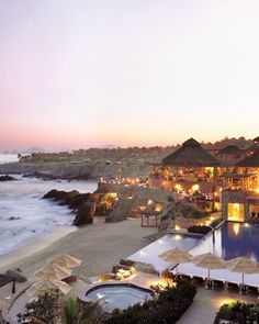 an outdoor swimming pool next to the ocean at dusk with umbrellas and chairs around it