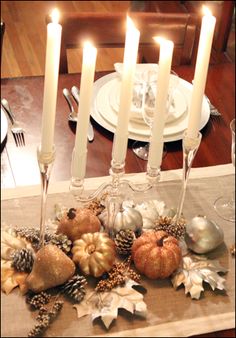 a dining room table with candles and decorations on it, including pine cones, acorns