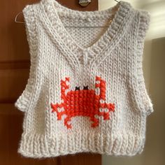 a knitted sweater with an orange crab on the front and bottom, hanging from a hook