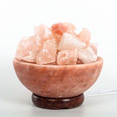 a wooden bowl filled with pink crystals on top of a white table next to an electric charger