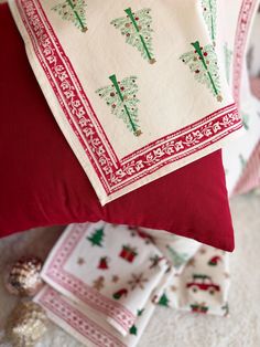 two red and white pillows with christmas trees on them next to other holiday napkins