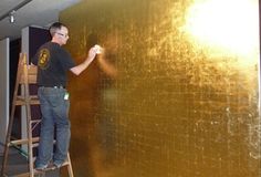 a man standing on a ladder painting a gold wall