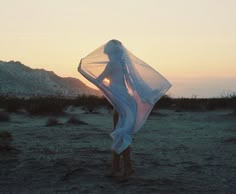 a woman is standing in the desert at sunset with her veil draped over her head