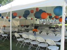 tables and chairs are set up under a tent with paper lanterns hanging from the ceiling