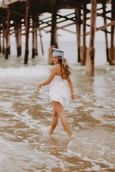 a woman in a white dress and goggles walking into the ocean near a pier