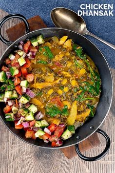 a pan filled with vegetables sitting on top of a wooden table next to a spoon