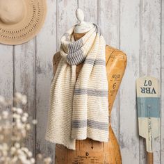 a white and gray scarf sitting on top of a wooden mannequin next to a hat