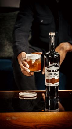 a man is holding a glass filled with ice cream and syrup next to a bottle of liquor