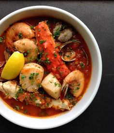 a white bowl filled with seafood and clams in tomato sauce, garnished with parsley