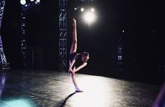 a woman is doing a trick on the dance floor in front of some bright lights