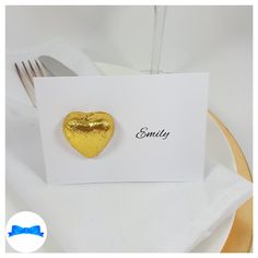 a gold heart shaped brooch sits on top of a white card next to a fork and knife