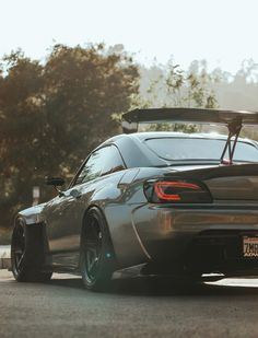 a grey sports car parked on the side of the road in front of some trees