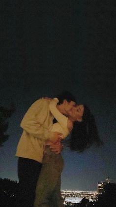 a man and woman kissing in front of the city at night