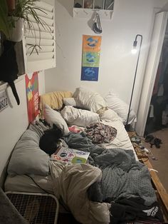 an unmade bed in a messy room with clothes on the floor and plants hanging above