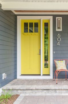 a yellow door sits in front of a gray house with two chairs on the porch