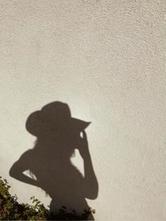 a shadow of a woman wearing a hat on the side of a building with flowers in front of her