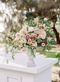 a vase filled with lots of flowers sitting on top of a white table covered in greenery