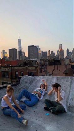 three people sitting on top of a roof talking on their cell phones in front of the city skyline