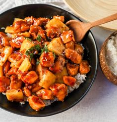 a black bowl filled with chicken and rice next to a wooden spoon on top of a table