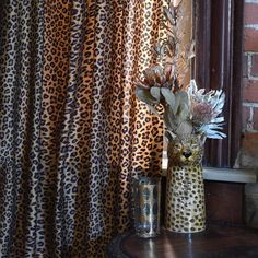 two vases with flowers on a table in front of a window covered by curtains