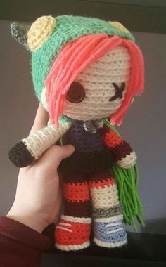 a hand holding a small crocheted doll with pink hair and green, red, white, and blue dreadlocks