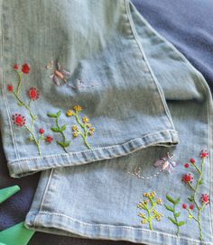 two pieces of denim with embroidered flowers on them and green scissors next to each other