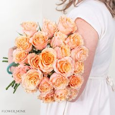 a woman holding a bouquet of peach colored roses