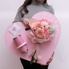 a woman is holding a pink heart shaped box with flowers and a cup on it