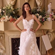 a woman standing in front of a fire place wearing a white dress with flowers on it