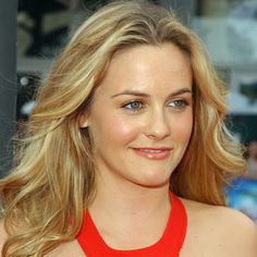 a close up of a person wearing a red dress and smiling at the camera with people in the background