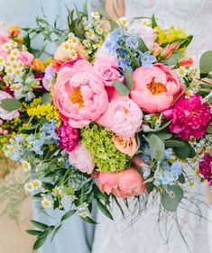 a bride holding a colorful bouquet of flowers in her hands and wearing a wedding dress