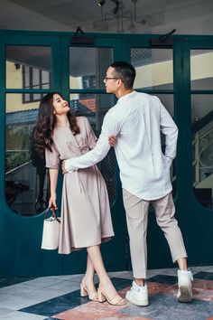 a man standing next to a woman in front of a green door and holding hands