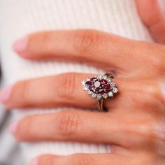 a woman's hand with a ring on it that has a red and white diamond center