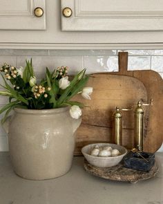 a white vase filled with flowers sitting on top of a counter next to a cutting board